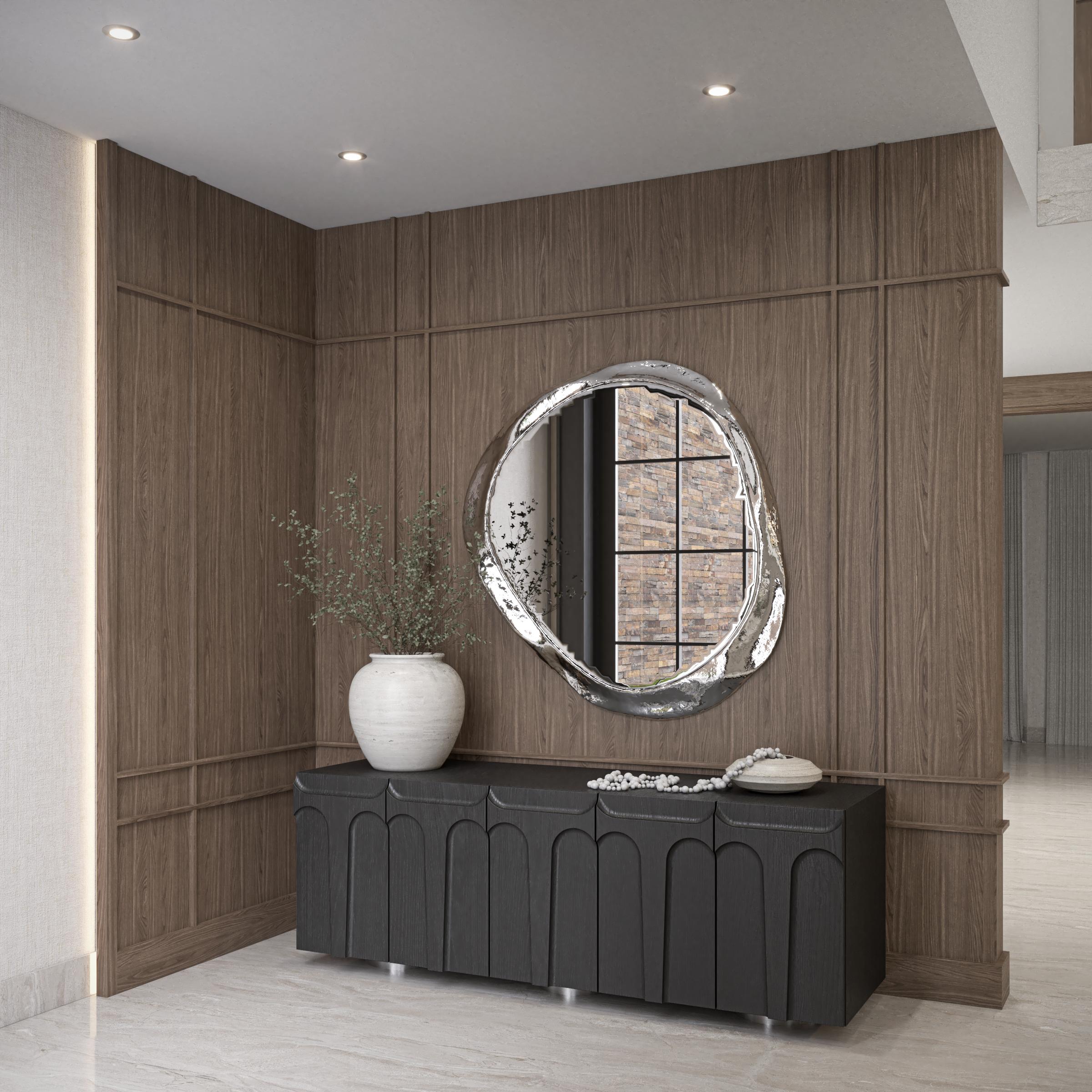 Vestíbulo con lambrín de madera, espejo de forma orgánica y credenza negra sobre piso de mármol desert, Casa Corteza, Mexicali, Baja California